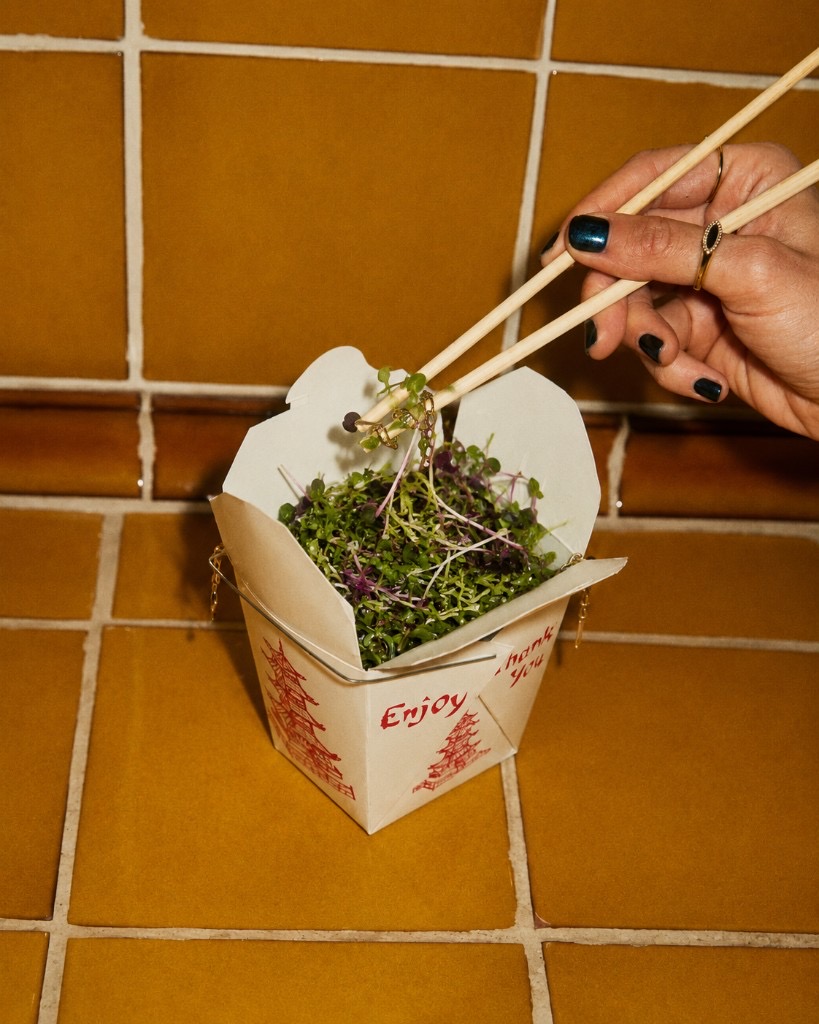 Hand lifting topiq microgreens from a takeout box