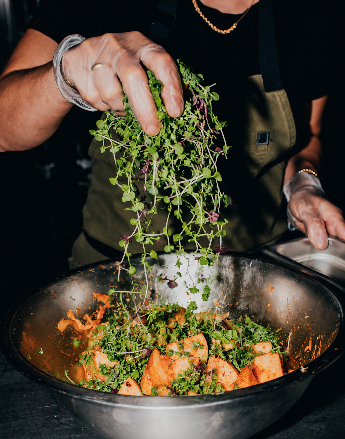 Chef tossing microgreens into a mixing bowl